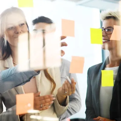 Three colleagues grouping sticky notes on a glass wall.