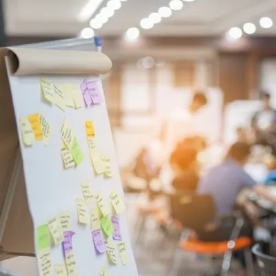A workshop flip chart covered in sticky notes, with participants seated behind it.